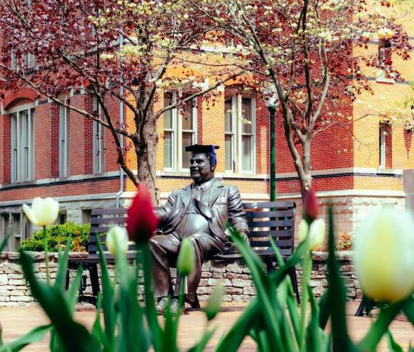 The Herman B Wells statue wearing a graduation cap on a spring day