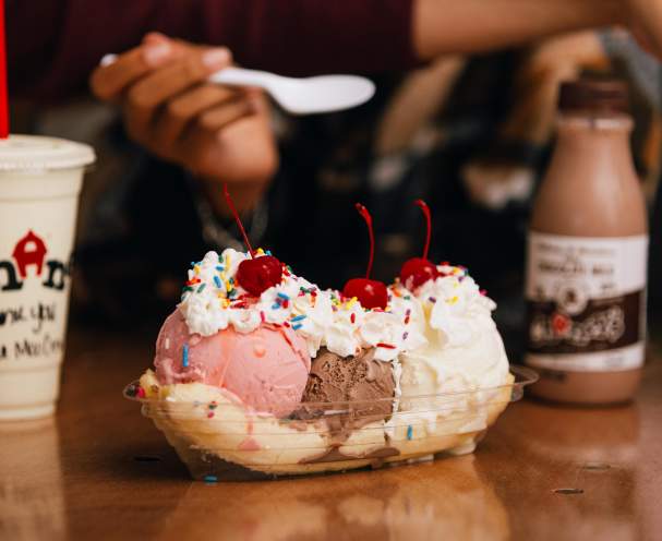 A banana split alongside a vanilla milkshake and a bottle of chocolate milk.