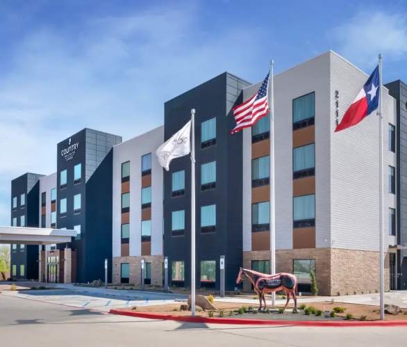 modern Country Inn & Suites hotel exterior in Amarillo with American and Texas flags waving outside beneath a wide blue Texas sky.