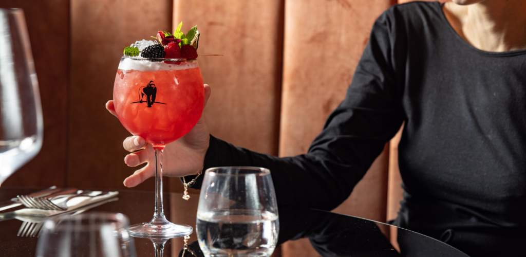 Close up of someone holding a red colour cocktail in a round glass with stem