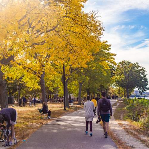 People sitting on benches and others walking on paved path along the Charles River Esplanade of Boston