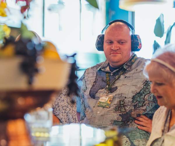A customer wearing noise‑reducing headphones receives support while visiting an accessible café, highlighting sensory‑friendly environments and inclusive dining options
