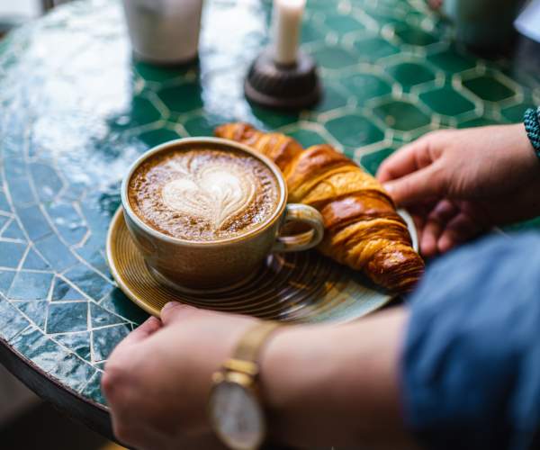 Kaffekopp med hjerteskum og en croissant servert på ett bord