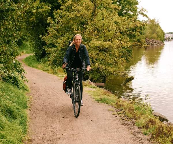 Kvinne som sykler langs en gruslagt vei på Glommastien, med Glomma i bakgrunnen.