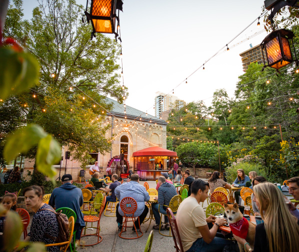 Lively outdoor patio at Colectivo Coffee on the Lake with colorful chairs, string lights, trees, and people dining under evening light.