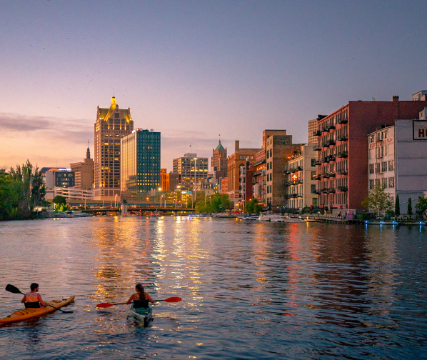 two kayakers on the Milwaukee River overlooking Milwaukee's Historic Third Ward and the skyline