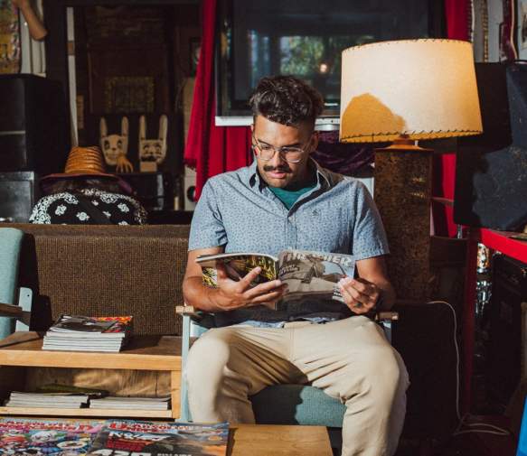 A person sits reading a magazine in a laid-back shop space with skateboards, posters, and eclectic vintage items.