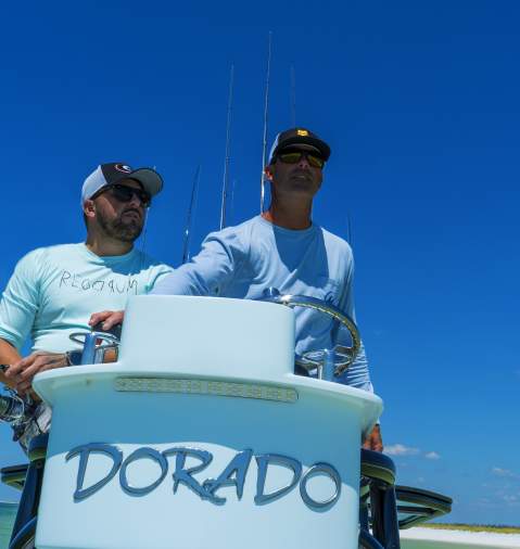 Two men headed out on fishing boat that says "Dorado"