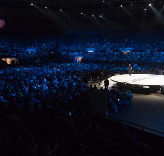Auditorium with a circular stage surrounded by a crowd.