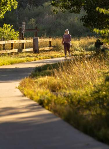Trail in Greeley with woman walking far in the distance with Visit Greeley and 250-150 logos