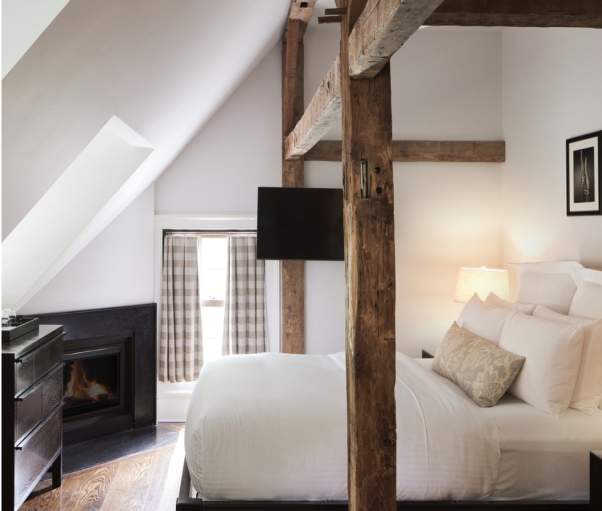 A guest room at the Bedford Post Inn. The room has wooden beams going over the bed and a fireplace can be seen in the background.