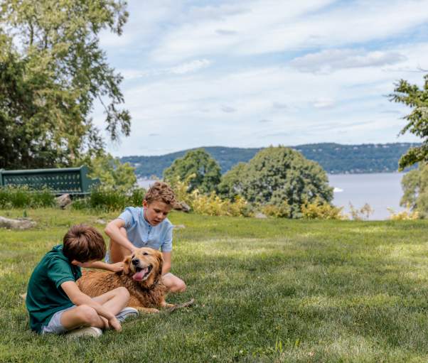 Two children pet a dog while sitting on the lawn of Lyndhurst, overlooking the Hudson River.