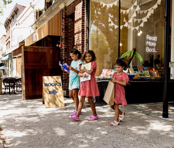 Three girls are holding books as they exit a store.