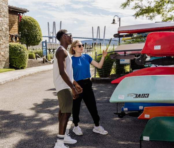 Two people stand next to a group of kayaking, getting ready to choose one and go out on the Hudson River.