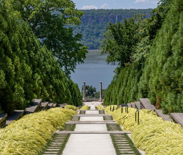 A line of green trees frames a pathway to the Hudson River.