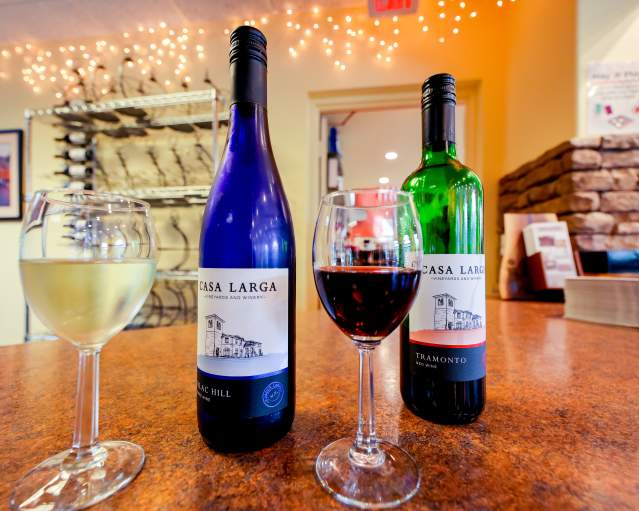 Two glasses of wine -- one white and one red -- sitting on a table in front of a blue bottle of Casa Larga wine and a green bottle of Casa Larga Wine at Casa Larga Winery