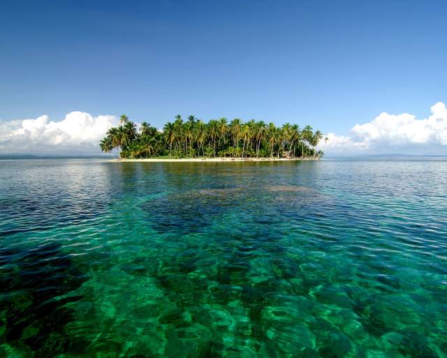 Small island covered in dense vegetation, with a few sandy beaches visible. The water is shallow and clear, with a visible sandy bottom.