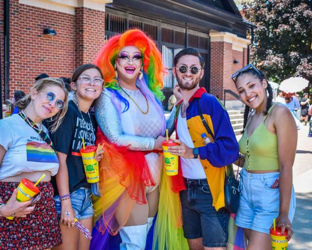 Four people posing with a drag queen at a street parade