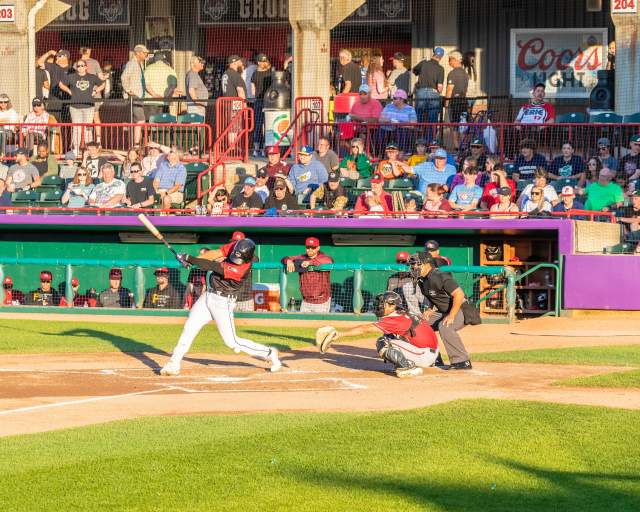 A baseball player swinging a bat in front of a dugout with people in the stands above