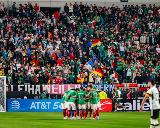 A huddle of soccer players in front of a goal in a crowd-filled stadium