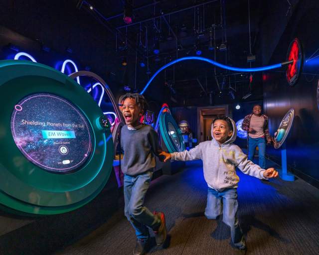 Two kids running around a dark display at the Franklin Institute