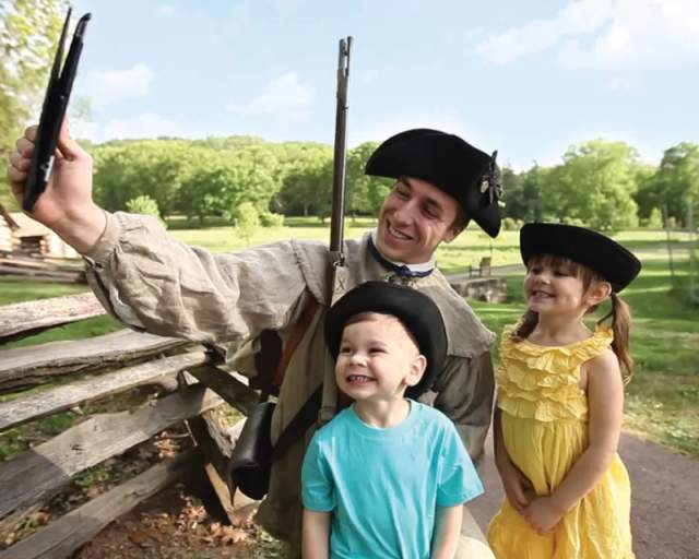 A man in a colonial costume taking a selfie with a young girl and boy