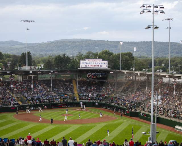 A baseball stadium filled with people watching a baseball game. A sign on the top of the stadium reads Welcome to Howard J. Lamade Stadium