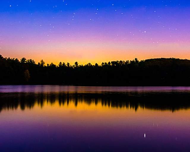 Blue and orange ombre night sky over a lake with trees