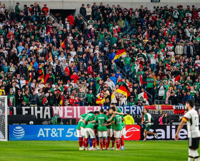 A huddle of soccer players in front of a goal in a crowd-filled stadium