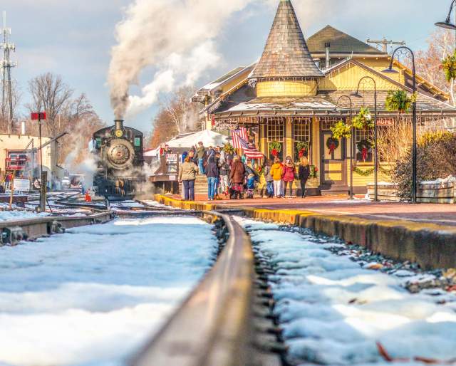 Close up of train tracks with the New Hope Railroad train blowing smoke and people getting on the train in the distance.