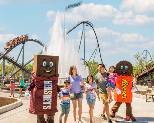 A family of five walking with two mascots in an amusement park