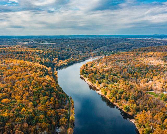 Aerial view of a river with two forests bursting with yellow, orange, brown, and green colored leaves on either side