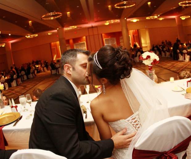 Back Shot of Couple Kissing at Reception with Guests Gathered Around Dance Floor in Background