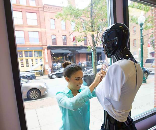 Young Woman Fixes Apparel on Manikin In Front of Glass Window