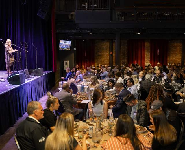 Kaitlin Eskelson standing at the podium addressing a full room of people seated at round tables