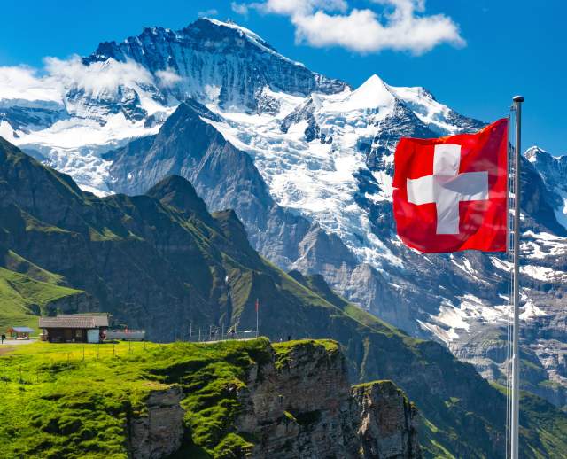 Swiss Alps - snow covered mountains with very green mountain meadow and a flag pole with the Swiss flag