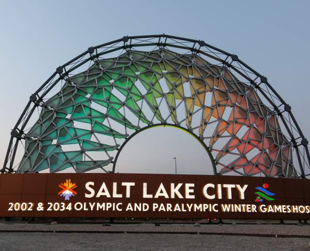 An arch of panels lit up in rainbow colors with Salt Lake City 2002 & 2034 Olympic and Paralympic Winter Games Host