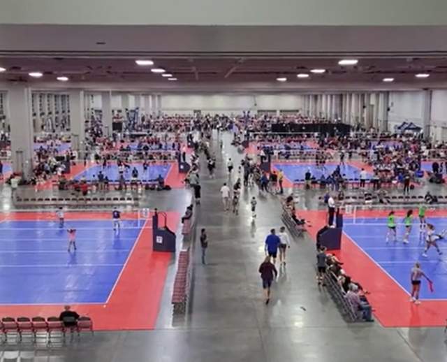 Indoor volleyball courts in a convention hall. Players are at each court with spectators