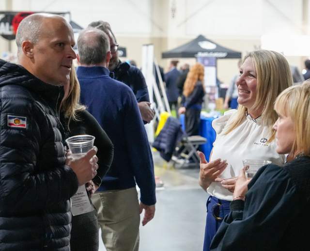 3 smiling people socializing with sports activities and booths in the background