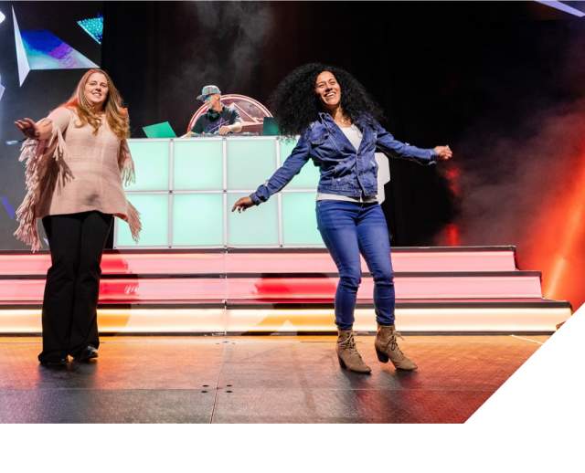 Two women standing on stage like they are presenting at a convention or meeting