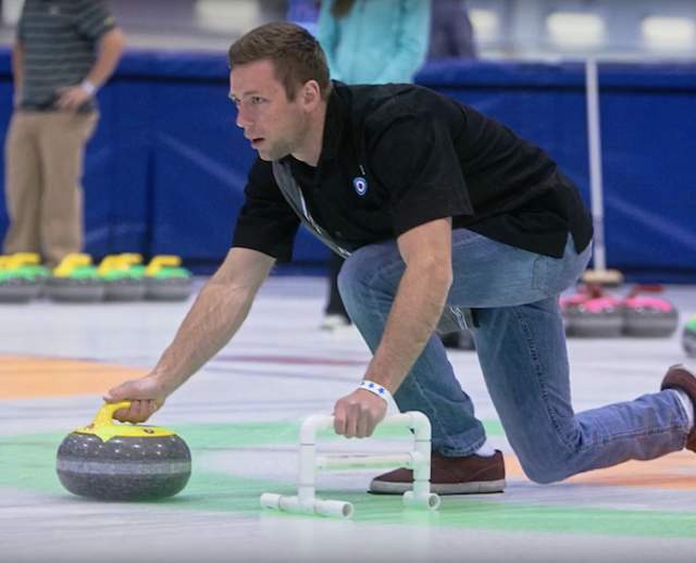 Man on one knee getting ready to send a curling stone on the ice at Utah Olympic Oval
