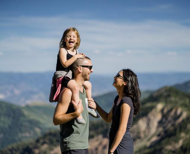 Man with happy child on his shoulders standing in front of a woman on a hiking trail mountaintop