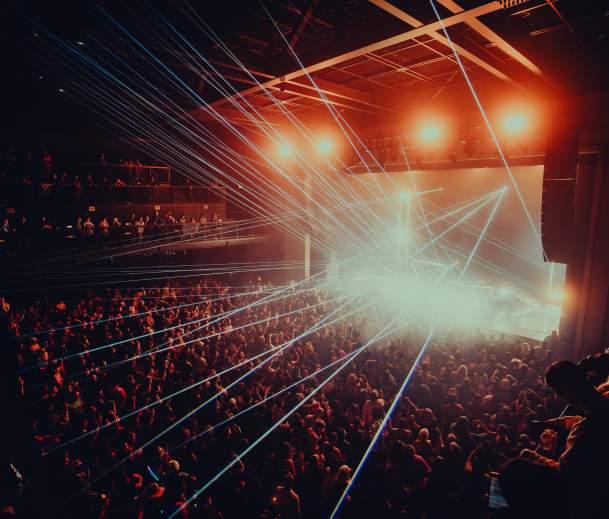 Crowd-filled concert at Channel 24 in Midtown Sacramento, with bright stage lights and blue laser beams illuminating the audience.
