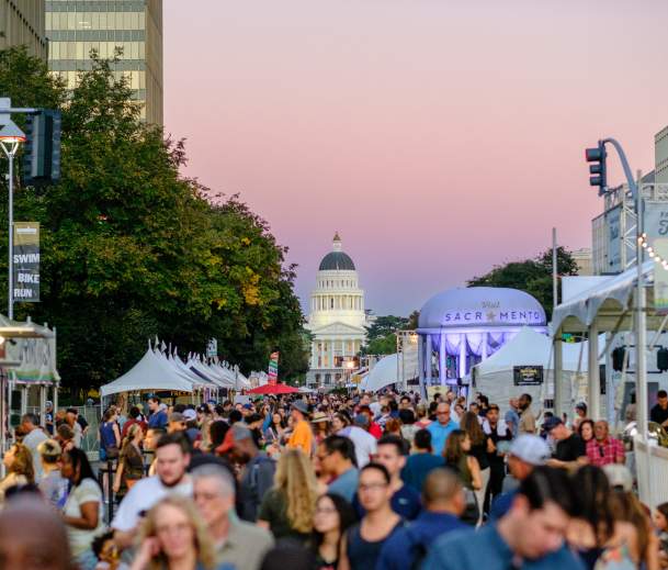a crowd walking around a festival at night with the capitol building in the background
