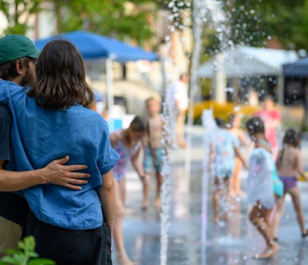 couple embracing as they watch kids splash in a fountain
