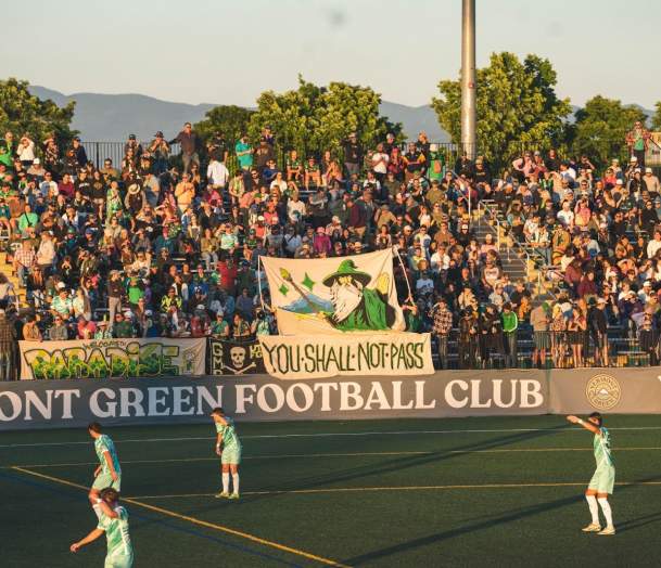 Vermont Green FC players on Virtue Field at sunset with the bleachers in the background.