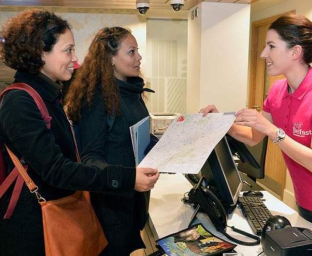 Woman in Visit Belfast welcome centre showing tourists a map of Belfast