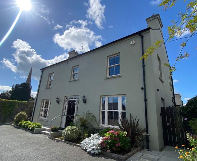 Exterior shot of Bramley House, a self-catering property in County Down.  There are plants outside the front of the house, and the sun is shining with blue skies.