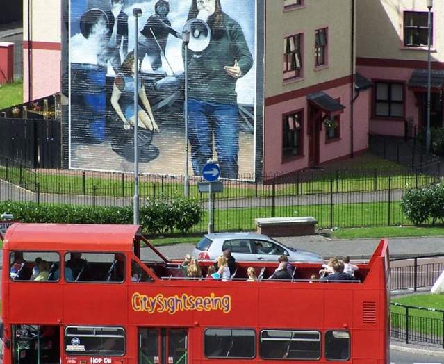 City Sightseeing Derry bus going past a wall mural in Derry