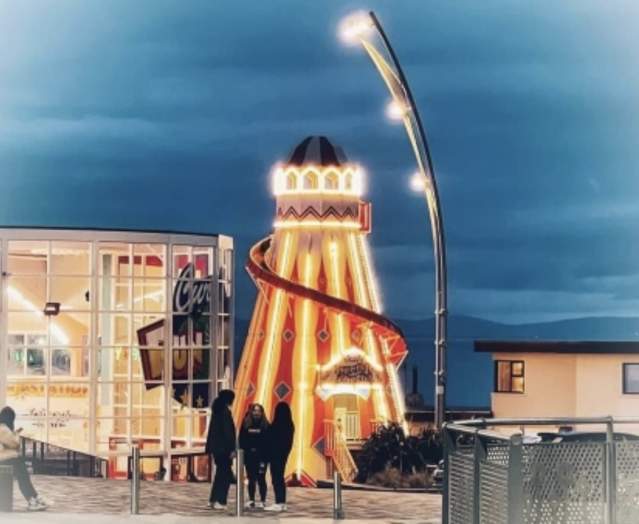 Exterior of Curry's Fun Park in Portrush with a group at the forefront and a Helter Skelter lit up in the background.